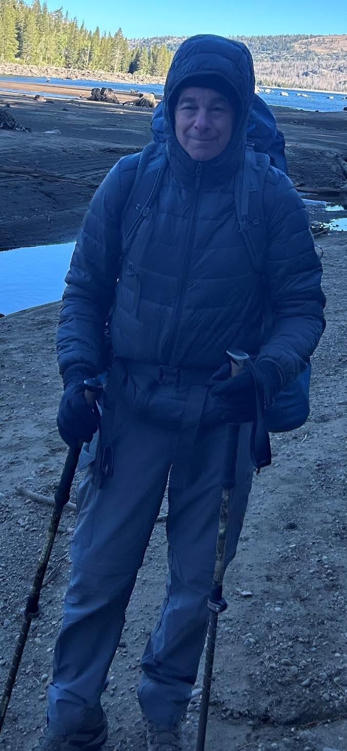 Anton in cold-weather backpacking gear with trekking poles near the Sierra campsite