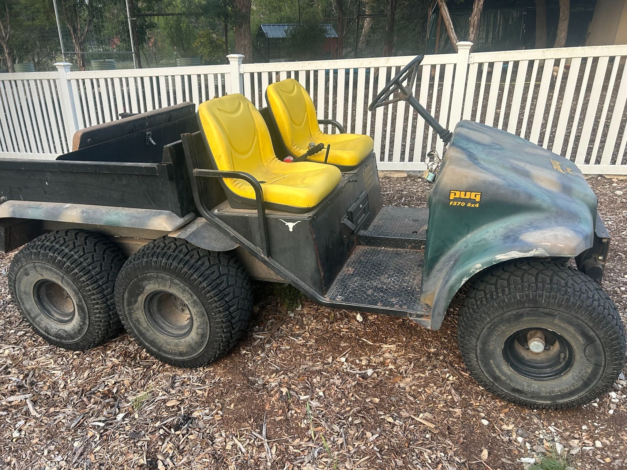 A Pug 6x4 all-terrain utility vehicle with a large dump bed, parked on a rural property.