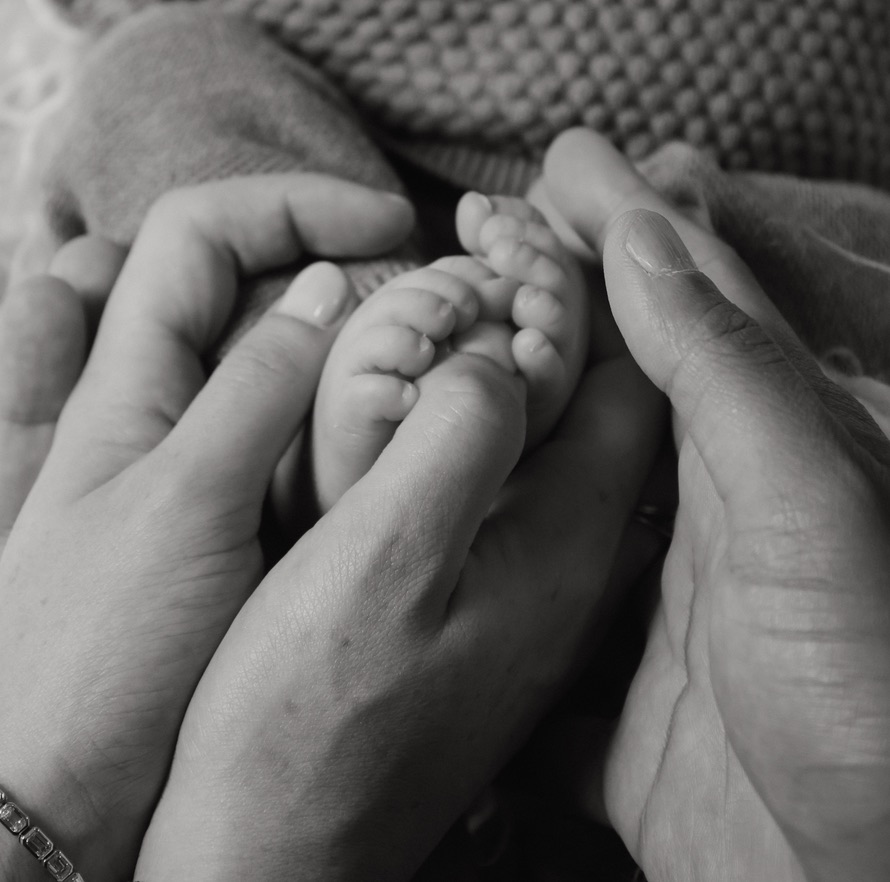 Parents' hands gently holding a newborn baby's feet